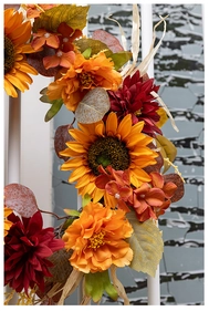Detail of autumn wreath featuring orange sunflowers and red dahlias with maple leaves