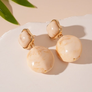 Detail of vintage beige resin earrings with marble texture on marble stand