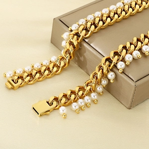 Macro detail of 18K gold Cuban link chain with white pearls on a beige jewelry box