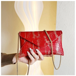 Detail of red crocodile pattern envelope clutch with golden chain strap for women
