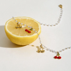Macro detail of a pearl necklace with red cherry pendants displayed on a fresh lemon slice