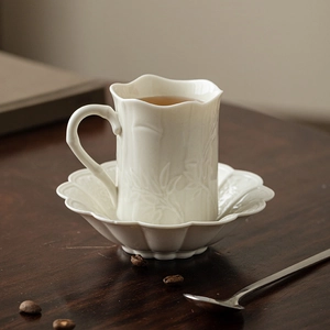 Ceramic coffee cup and saucer set with floral relief on a dark wooden table