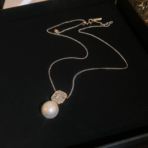 Détail macro d'un pendentif perle ronde avec zircon carré sur un collier doré