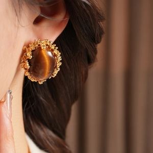 Close-up of model wearing vintage gold-toned earrings featuring an oval brown tiger eye stone