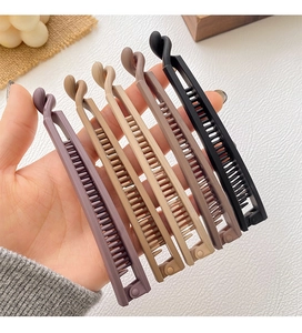 Close-up of five matte banana hair clips in assorted Morandi colors held by hand
