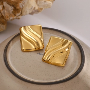 Macro shot of 18K gold plated square earrings with unique wave texture on a stone base
