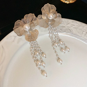 Detail of long tassel earrings with gold hollow flowers and faux pearl bead drops