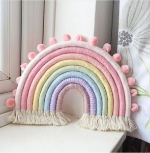 Close-up of handmade woven rainbow wall hanging with soft tassels and pink pom-poms