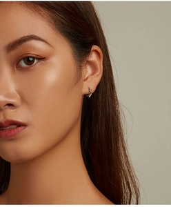 Close-up of elegant gold snake hoop earring with green zircon on a female model