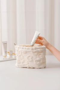 Detail of hand placing cosmetics into white floral plush makeup bag with zipper