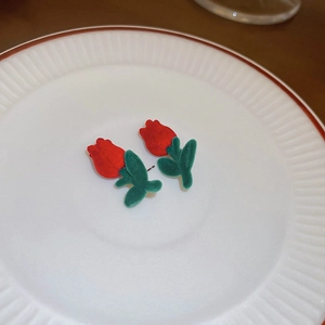 Close-up of red flocked tulip stud earrings with green leaves on a ceramic plate
