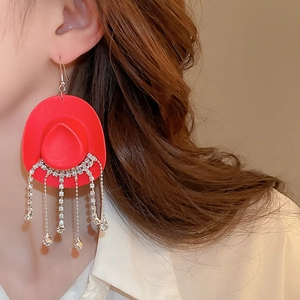 Detailed view of red cowboy hat earrings with sparkling tassels worn by a model