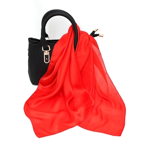 Detail of red satin scarf draped on black leather handbag showing smooth silk texture