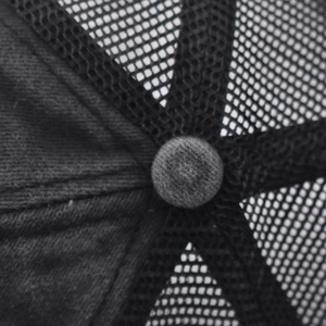 Macro detail of black mesh trucker hat top button and breathable stitching texture