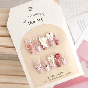 Pink gradient press-on nails with white bows, pearls, and angel relief on display card