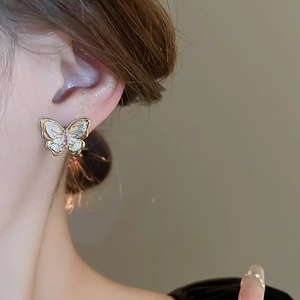 Détail d'une boucle d'oreille papillon dorée avec ailes blanches et zircon rose sur l'oreille