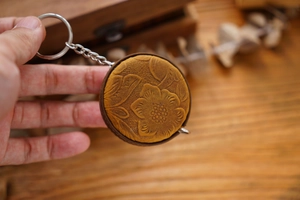 Close-up of hand holding a yellow embossed leather mini tape measure with floral pattern
