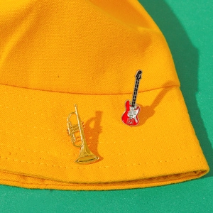 Musical instrument brooch set with gold trumpet and red guitar on a yellow canvas hat