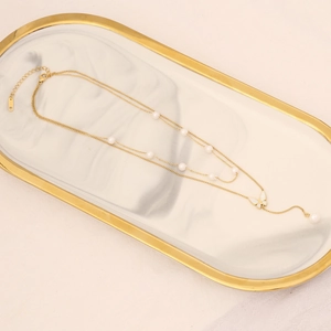 Detail view of a gold double-layer butterfly necklace with pearls on marble tray
