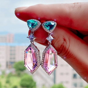 Elegant long drop earrings with pink and green 3A zircon crystals held by hand outdoors
