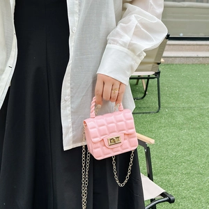 Pink quilted jelly handbag with gold chain strap and metal lock shown in outdoor garden