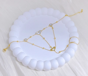 Detail of gold hand chain featuring heart shell, pearls, and adjustable lobster clasp