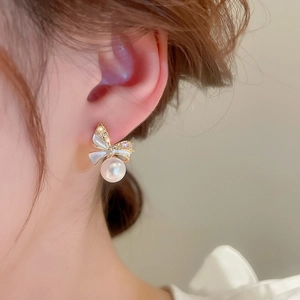 Detail of bow-shaped earring with pearls and diamonds shown on a model's ear