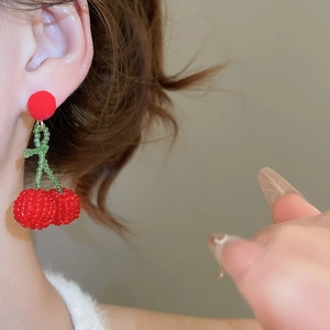 Close-up of cherry bead earrings with red plush pom pom worn by a female model