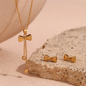 Close-up of gold bowknot tassel necklace and matching stud earrings on decorative props