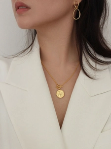 Close-up of a model wearing a gold OT toggle necklace with a round coin pendant and earrings