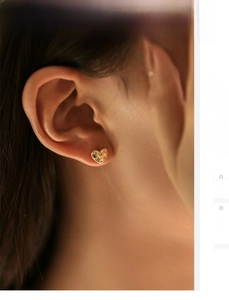 Close-up of golden heart-shaped stud earrings with shimmering rhinestones on ear