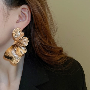 Close-up of oversized golden 3D flower earrings with elegant brushed metal texture