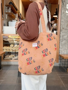Corduroy tote bag with orange Keep Smiling print shown on shoulder in shop scene