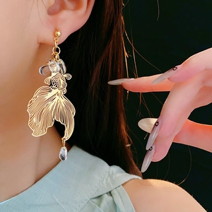 Detail of gold koi fish earrings with crystal teardrop bead worn by a model