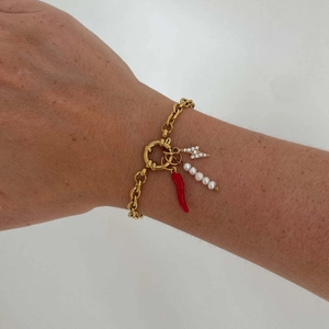 Gold chain bracelet with chili, pearl, and lightning pendants on a model's wrist