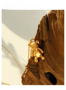 Detailed view of a 3D gold bear pendant hanging on dark wood with a delicate chain