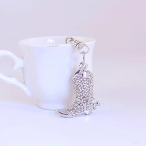 Elegant silver metal keychain with rhinestone studded cowboy boot pendant on a cup