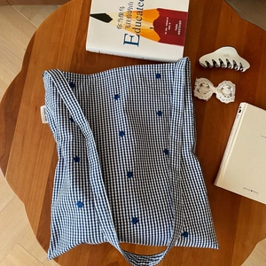 Détail du sac en coton à carreaux bleus et blancs avec broderie fleurie sur une table