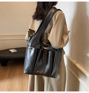 Close-up of a vintage black PU leather tote bag with multiple pockets on a beige trench coat