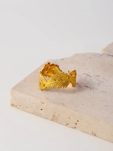 Detailed close-up of golden leaf-shaped ring with textured mesh on a stone base