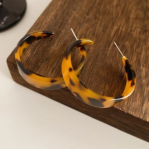 Close-up of tortoise shell resin C-shaped hoop earrings with metal posts on wooden display