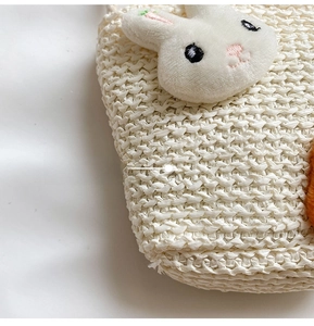 Dettaglio della paglia intrecciata e del coniglietto di peluche sulla borsa crema