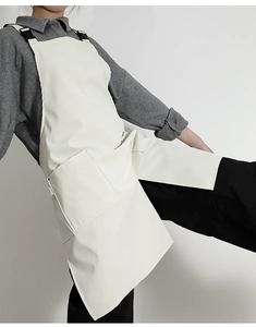 Detail of cream canvas apron featuring adjustable black buckle straps and large pocket