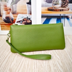 Detail of green litchi grain leather wallet with matching wrist strap on wood