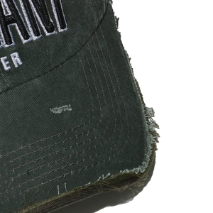 Macro view of vintage embroidered letters and distressed frayed edges on dark green baseball cap