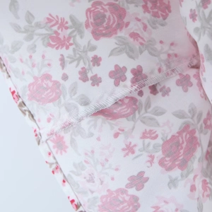 Detailaufnahme des rosa Blumenmusters auf weißem Stoff mit präziser Nahtverarbeitung