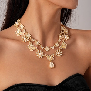 Detail of layered gold necklace with butterfly flower charms and teardrop crystal pendant