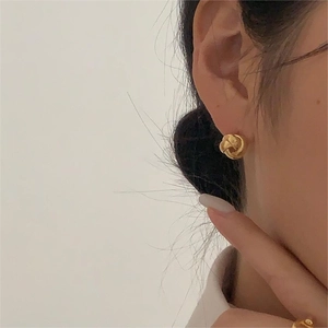 Orecchini a perno attorcigliati in oro opaco dal design minimalista indossati da modella