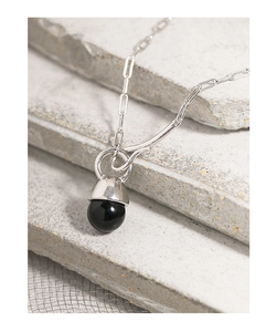 Macro shot of silver paperclip chain necklace with a black onyx pearl pendant on stone