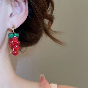 Close-up of model wearing red grape-shaped resin bead earrings with green leaf detail